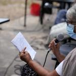 mujer sentada hablando por un  microfono leyendo de un cuaderno