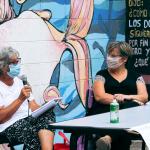 dos mujeres sentadas una de ellas hablando por un microfono