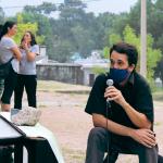 hombre sentado hablando por microfono y tres mujeres al fondo