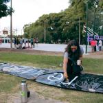 mujer pintando una pancarta con gente haciendo ejercicios al fondo en una cancha