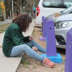 mujer sentada en el piso pintando pinos de estacionamiento pintados de colores