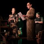 Fotografía de la obra Laberinto, tres actrices en escena, una lee un papel, una a su lado la observa y otra atrás habla.