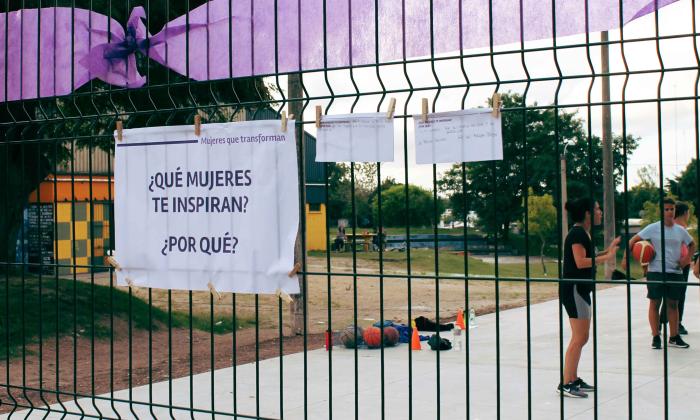 Hoja de tamaño a 3 colgada en una reja adelante de una cancha con la inscripción que mujeres te inspiran y porque?