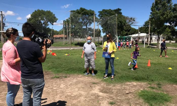 Una periodista habla con un referente de SACUDE frente a una cámara en la cancha del complejo