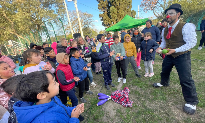 grupo de niños y niñas rodeando a un señor con nariz de payaso que hace malabares