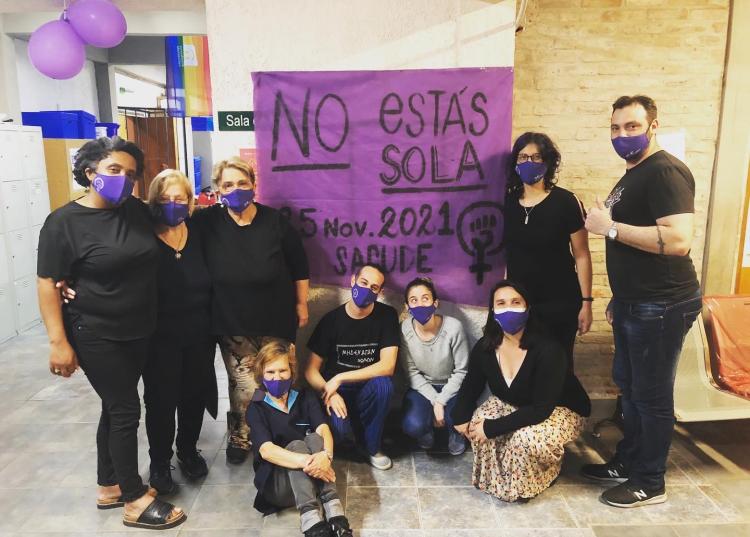 9 Personas posan vestidas de negro frente a un cartel que dice no estás sola