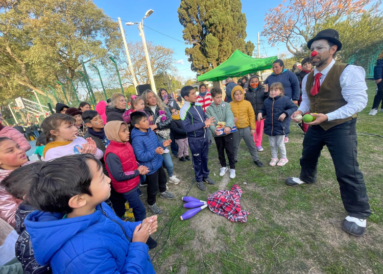 grupo de niños y niñas rodeando a un señor con nariz de payaso que hace malabares