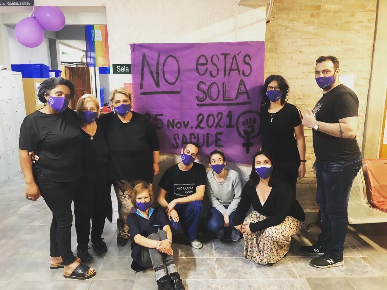 9 Personas posan vestidas de negro frente a un cartel que dice no estás sola