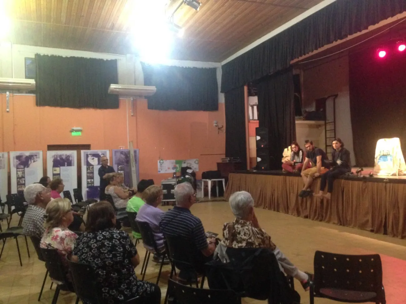 Una actriz y un actor están sentados en el escenario conversando con el público