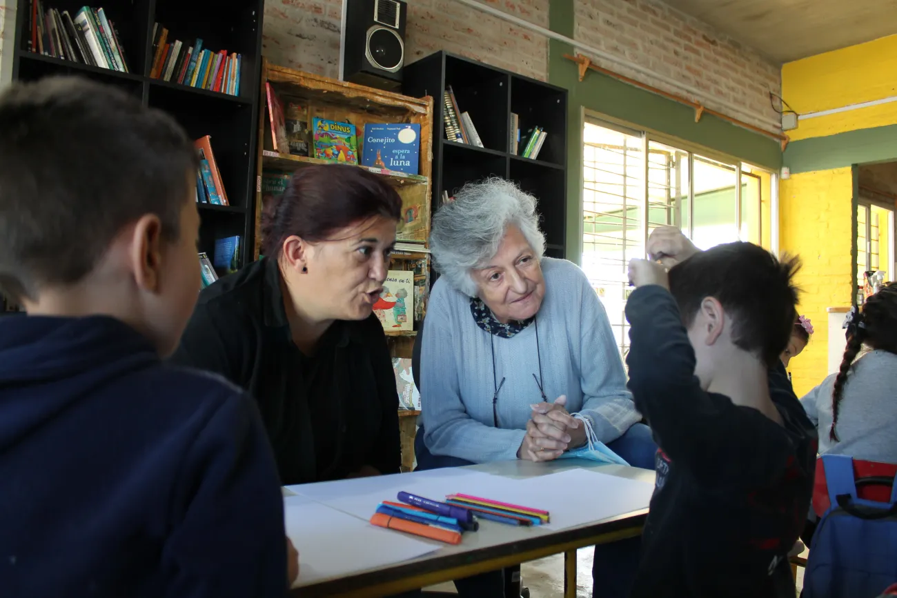 Personas mayores intercambian con niñas y niños en el hall del complejo