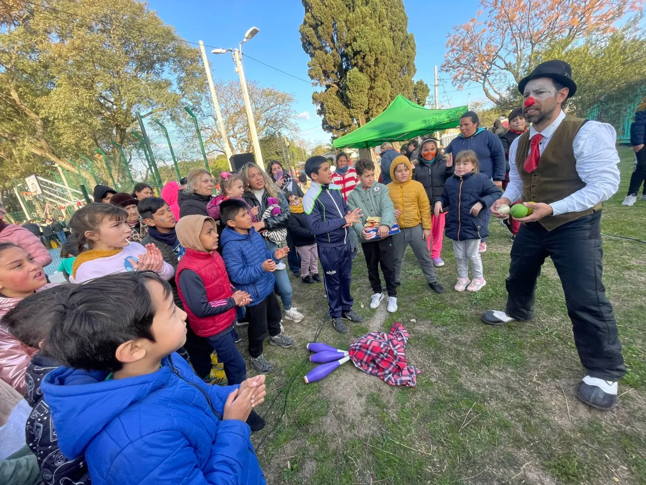 grupo de niños y niñas rodeando a un señor con nariz de payaso que hace malabares